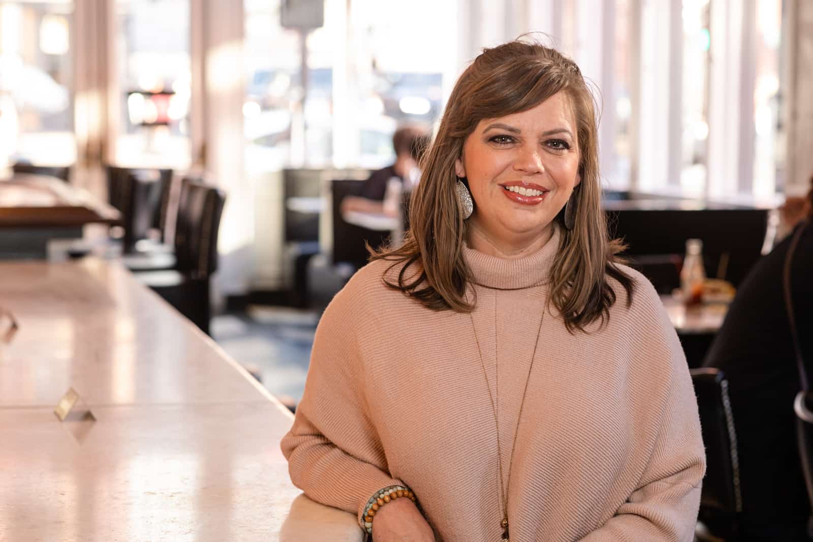 Woman in pink sweater smiles inside restaurant